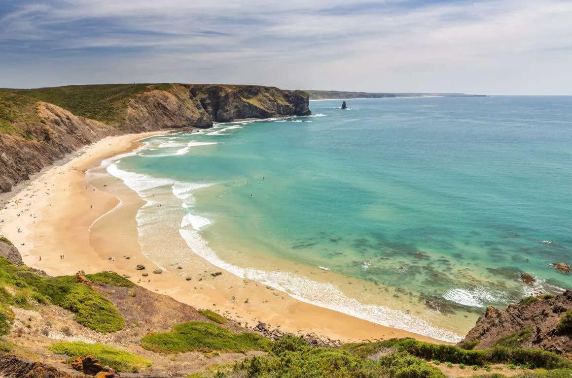 Cliff view of Praia da Arrifana bay with golden sand and dramatic cliffs in Aljezur, Algarve